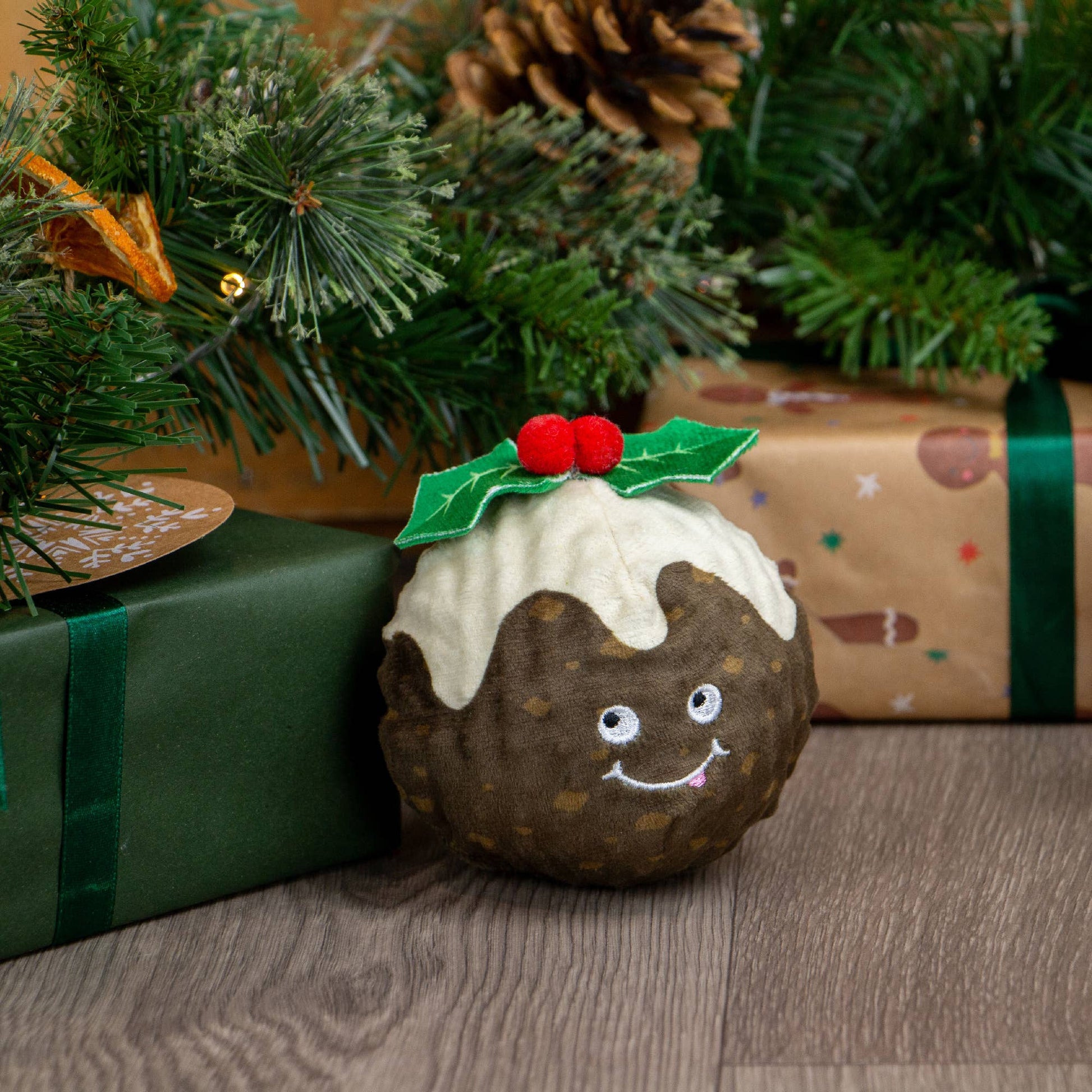 Toy resembling a Christmas pudding with a face, surrounded by Christmas decorations and presents.