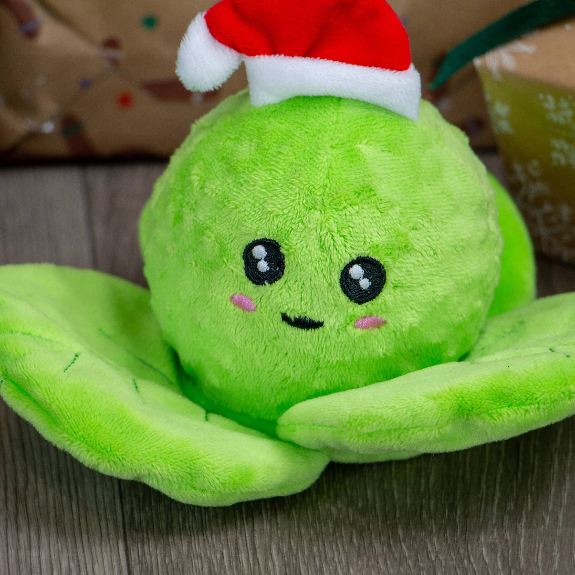 Green plush toy with a Santa hat on a wooden surface