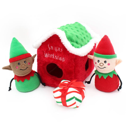 Two elf plush toys and a red 'Santa's Workshop' toy house on a white background